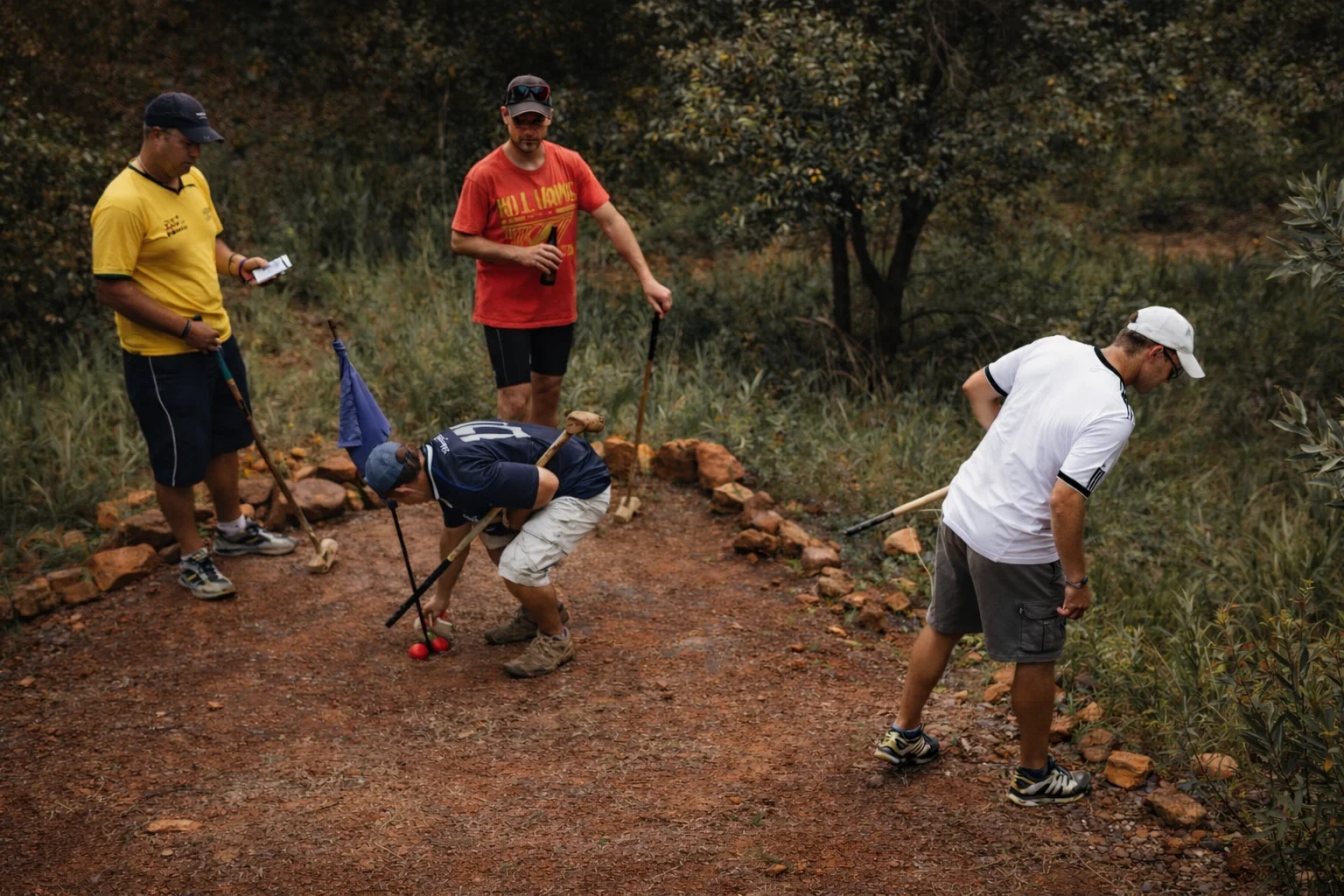 A group of friends laughing around a red ball and blue flag on the Ancient Golf course at Shelter Rock, knobkieries in hand.