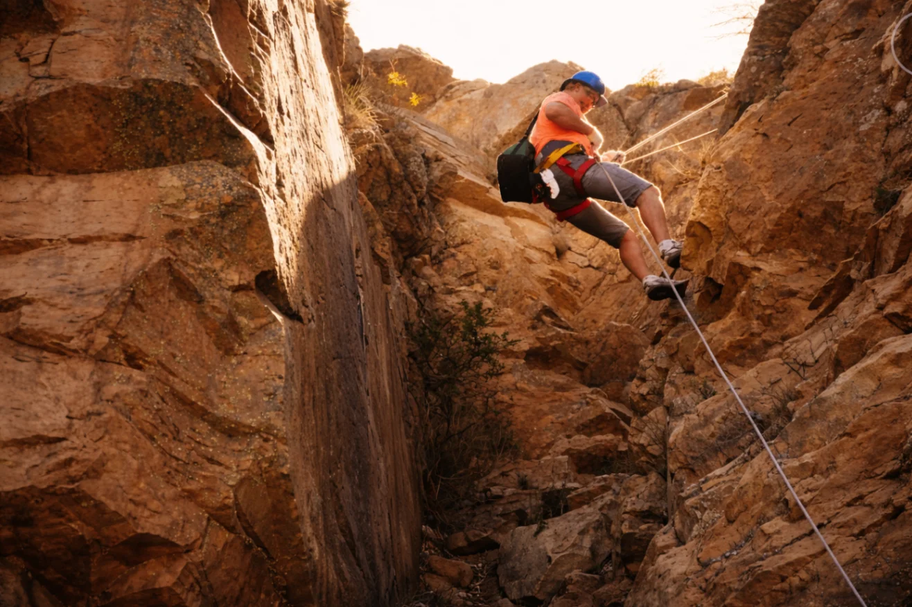 Abseiler descending a rugged Magaliesberg sandstone cliff on rope in warm golden light.