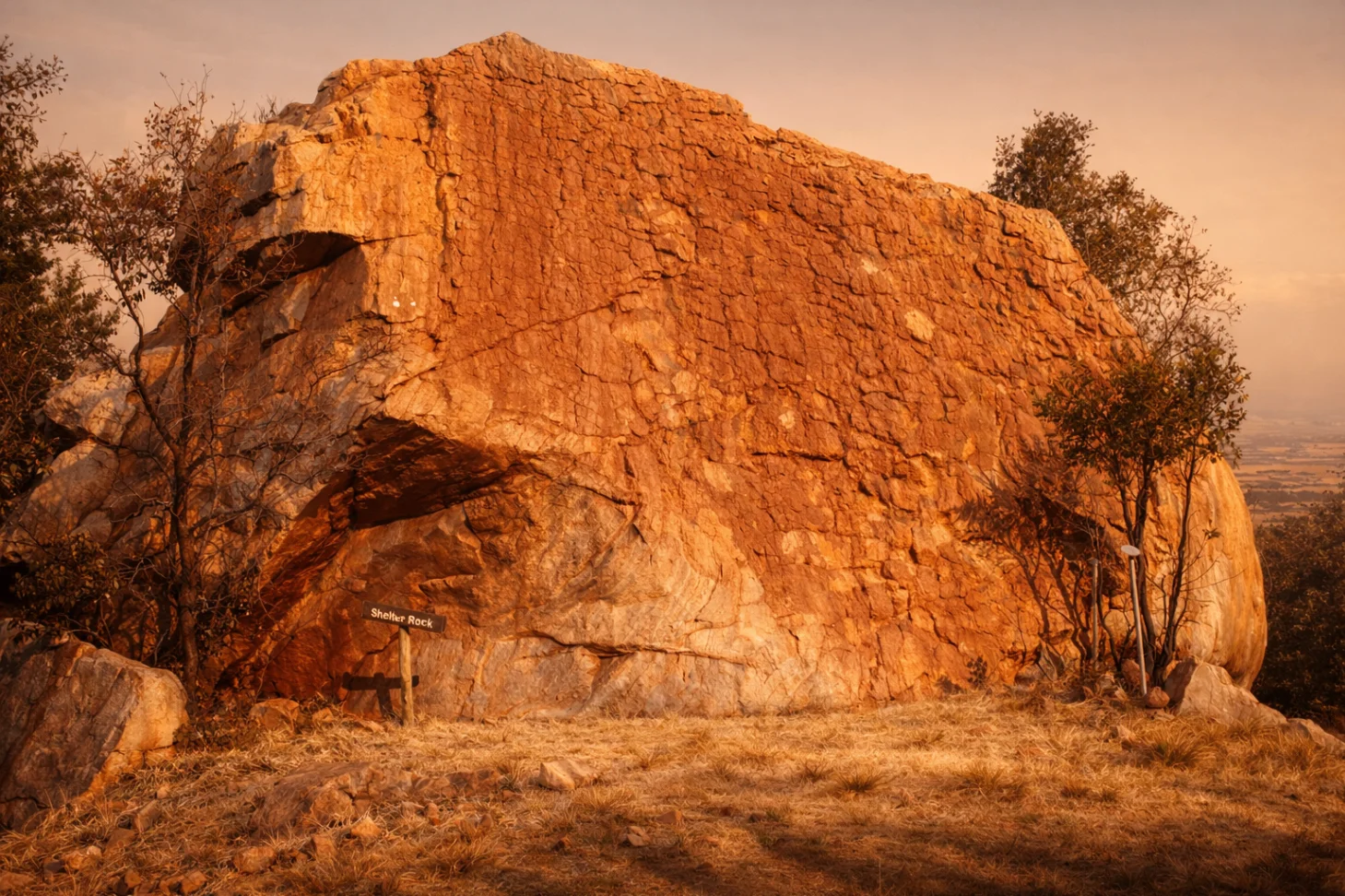 The vast Shelter Rock sandstone formation glowing in warm sunset light with a small trail signpost at its base.