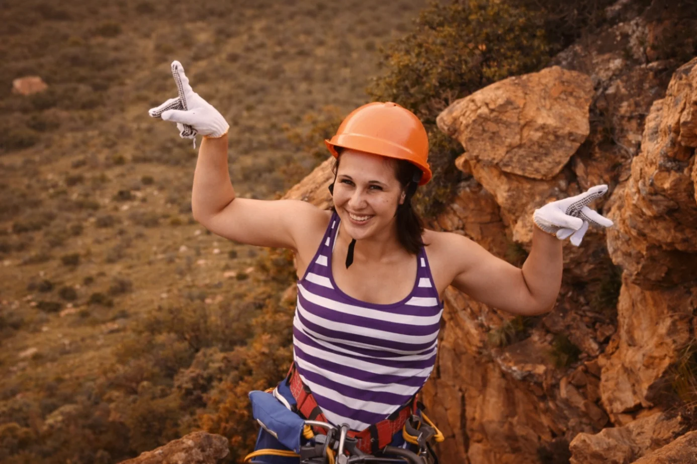 Abseiler on the Magaliesberg cliff smiling with arms raised after the descent.